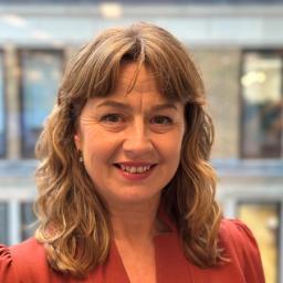 Professional headshot of Sophie White, a woman facing the camera with a neutral background, dressed in smart casual attire and smiling softly.