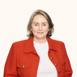 Smiling woman with gray hair in a bright orange jacket.