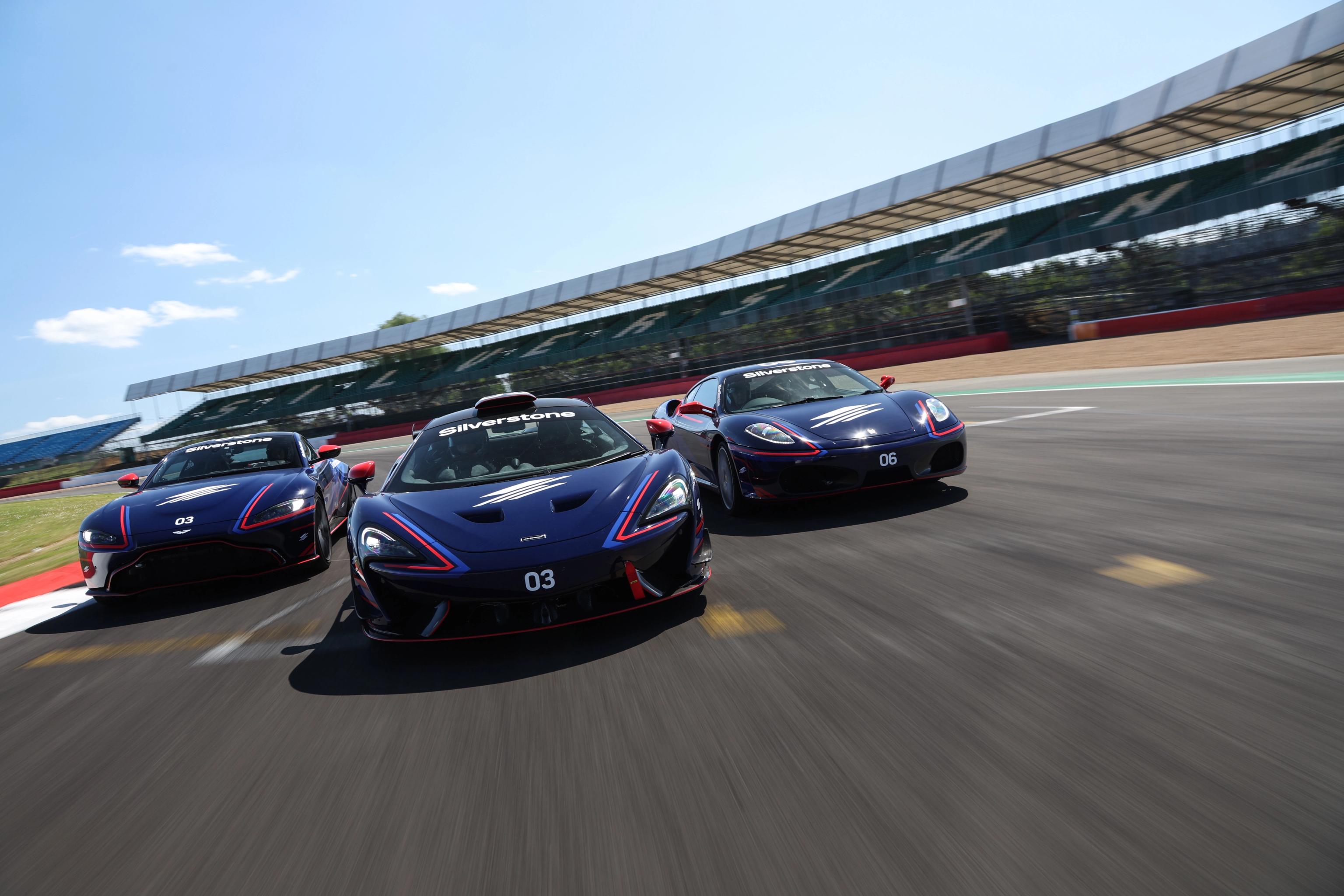 Three blue sports cars with red and white accents racing on a track at Silverstone.