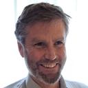 Smiling man with grey hair and a beard, wearing a light shirt.