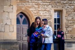 Two women look at a brochure in front of a stone building.
