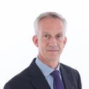 A man with grey hair and blue eyes, wearing a dark pinstripe suit and purple tie.