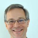 A smiling man with gray hair and glasses, wearing a black and red robe.