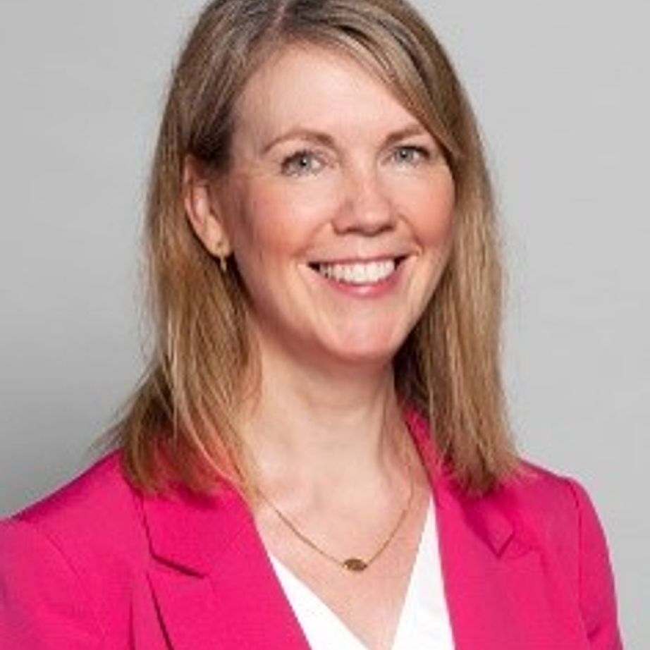 Headshot of a smiling woman with blonde hair wearing a pink blazer.