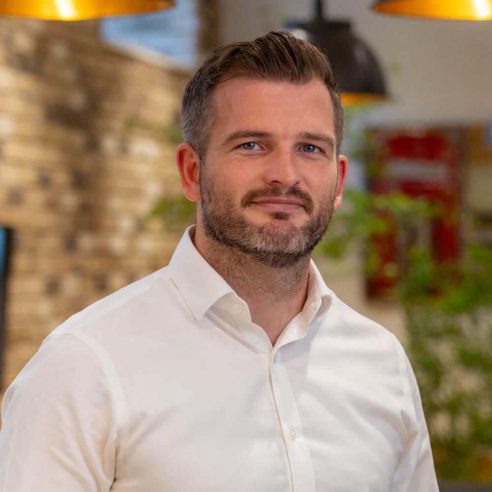 Headshot of a man with a beard and a white shirt smiling.