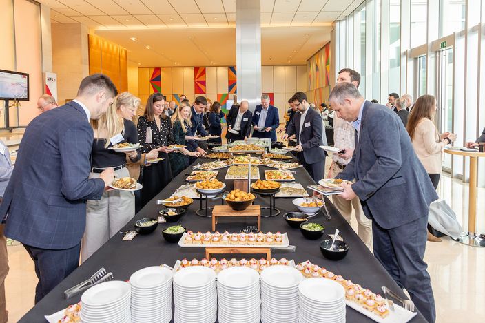 a group of people are standing around a long table with plates of food .