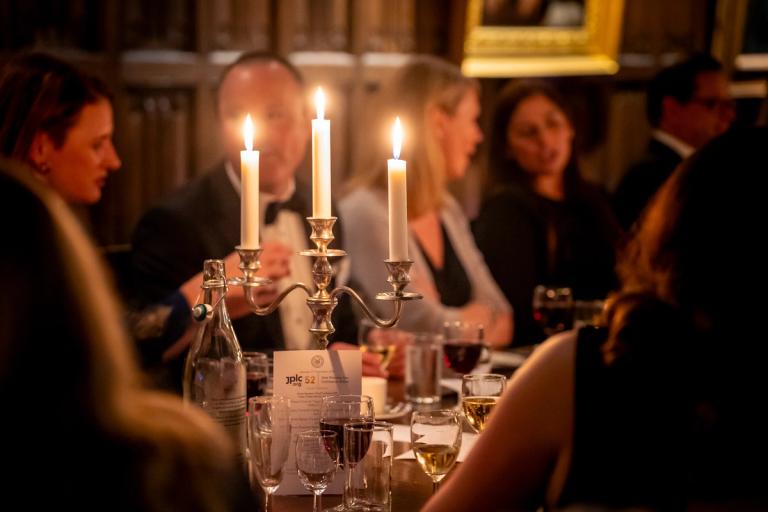 A candlelit dinner with a candelabra on a table surrounded by seated guests.