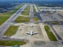 Aerial view of an airport with multiple airplanes on runways and tarmac, and a control tower in the distance.