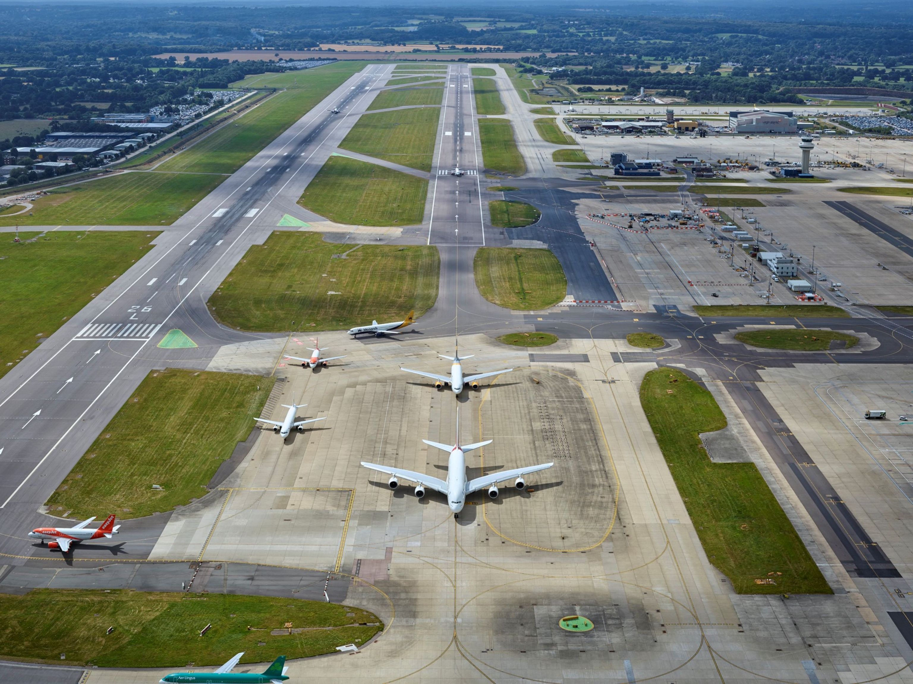 Aerial view of an airport with multiple airplanes on runways and tarmac, and a control tower in the distance.