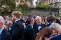 An outdoor gathering of people in formal wear, with an older man in a tuxedo smiling.