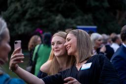 Two smiling women pose for a selfie at an outdoor event.