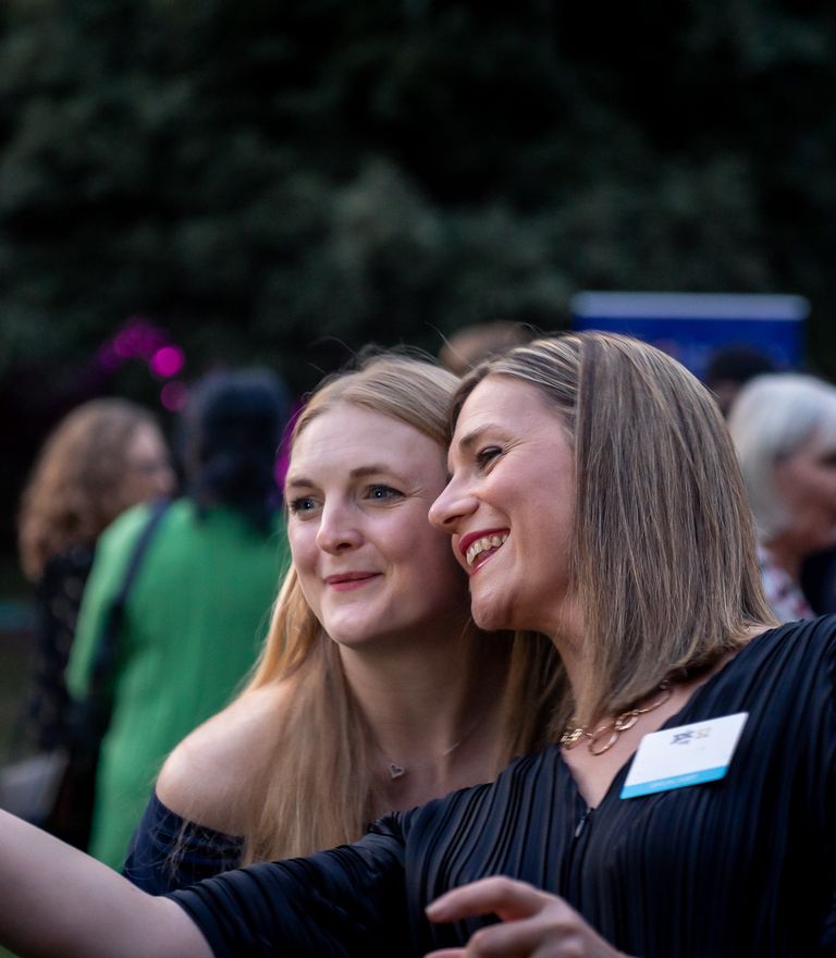 Two smiling women pose for a selfie at an outdoor event.