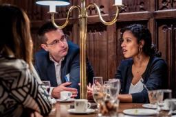 Three people in conversation around a table in a formal, wood-paneled room.