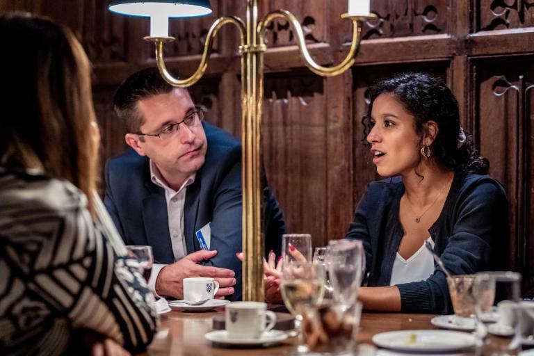 Three people in conversation around a table in a formal, wood-paneled room.