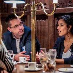 Three people in conversation around a table in a formal, wood-paneled room.