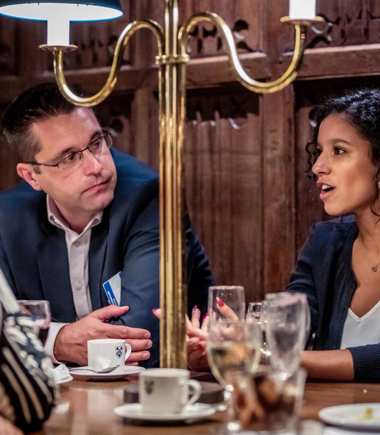 Three people in conversation around a table in a formal, wood-paneled room.