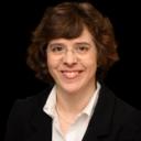 A smiling woman with short brown hair and glasses, wearing a black blazer and pearl necklace.