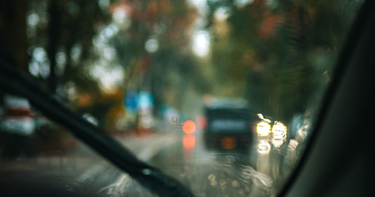CarPlay Weather Widget: How to Add, Fix, and Pin the Forecast in iOS 26 — View through a rainy windshield at blurred traffic lights