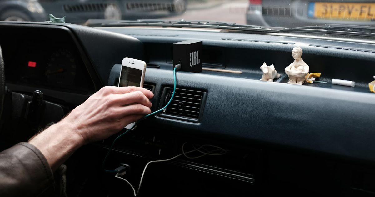 Phone Charging But CarPlay Not Working? The 4-Test Fix (iOS 26) — person hand holding iPhone on dashboard during daytime
