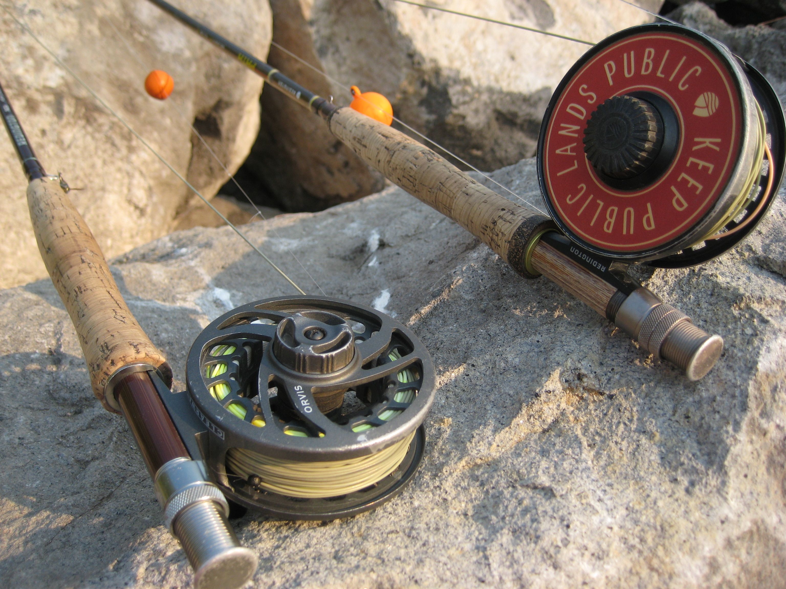 Two fly rods and reels resting on rocks, including a reel marked Keep Public Lands Public