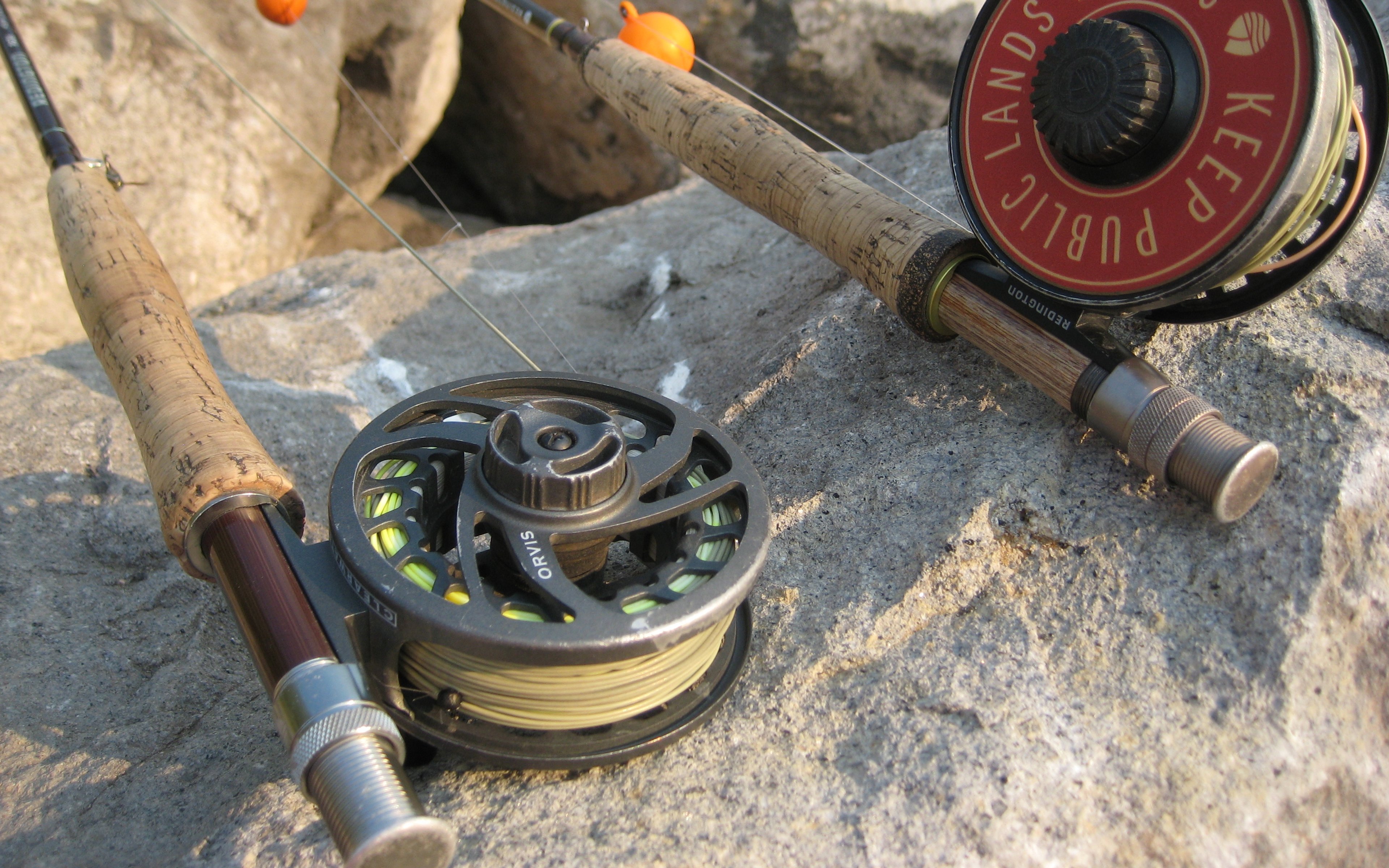 Two fly rods and reels resting on rocks, including a reel marked Keep Public Lands Public