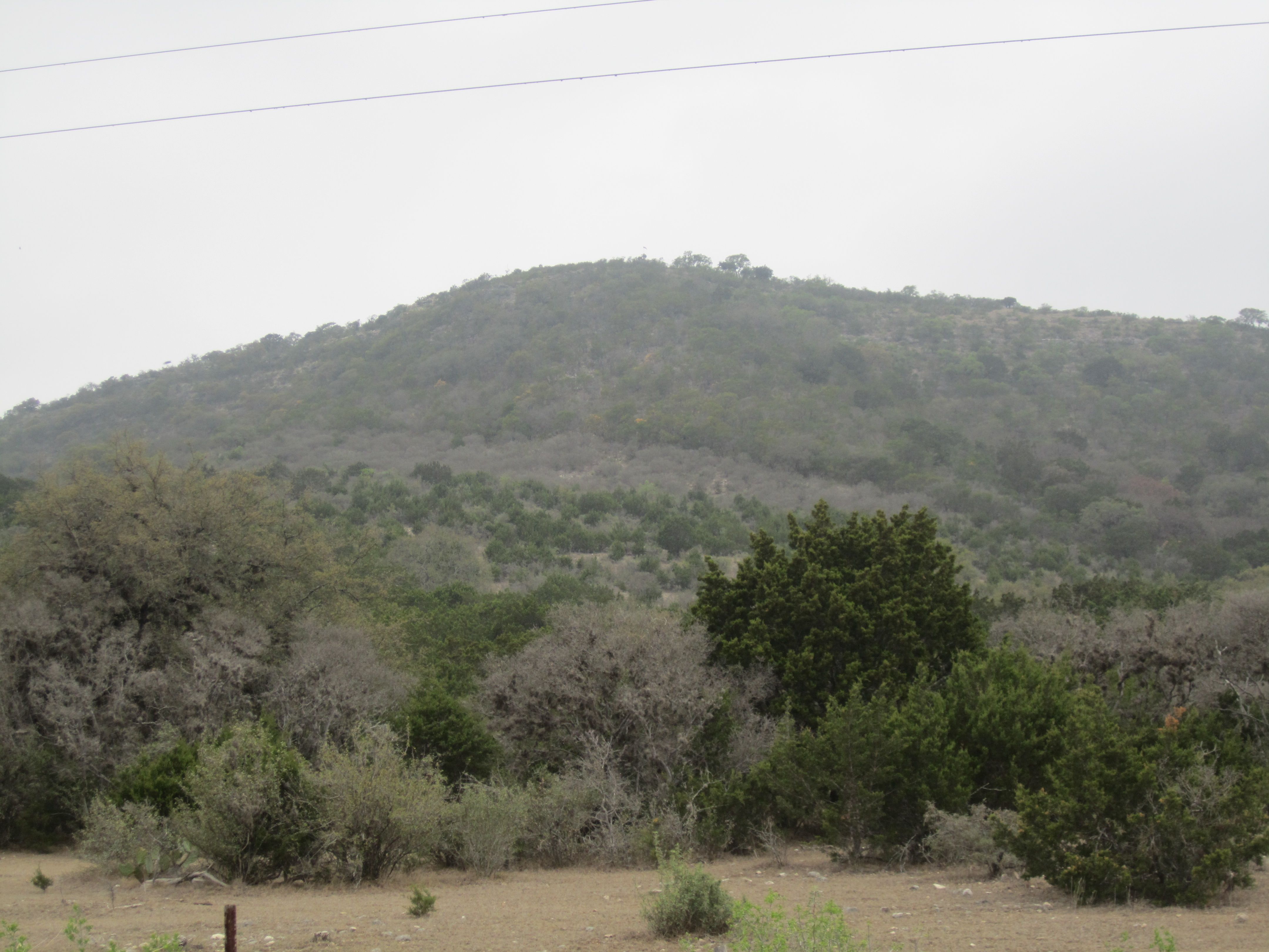 A scenic Texas Hill Country landscape of rolling, oak-covered terrain.