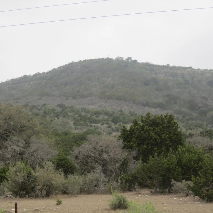 A scenic Texas Hill Country landscape of rolling, oak-covered terrain.
