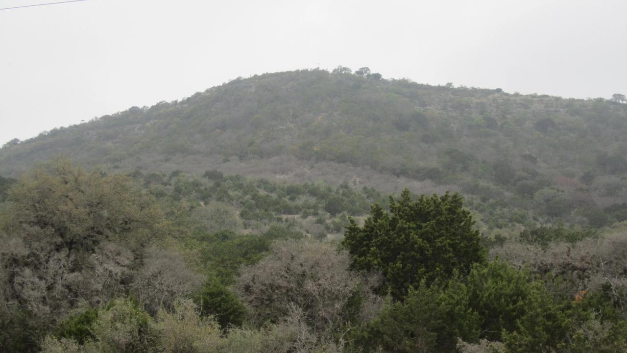 A scenic Texas Hill Country landscape of rolling, oak-covered terrain.