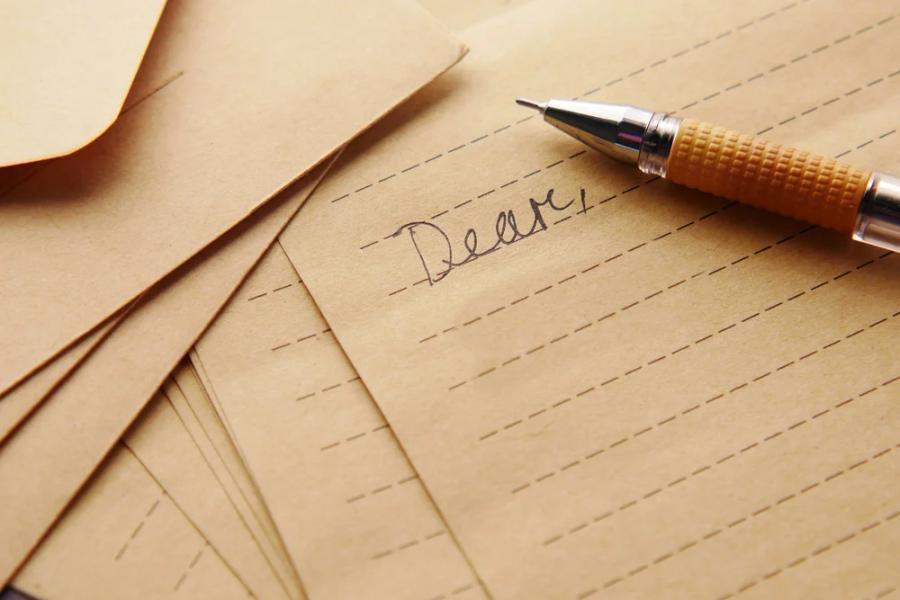 A handwritten letter beginning “Dear,” with a pen resting on lined paper