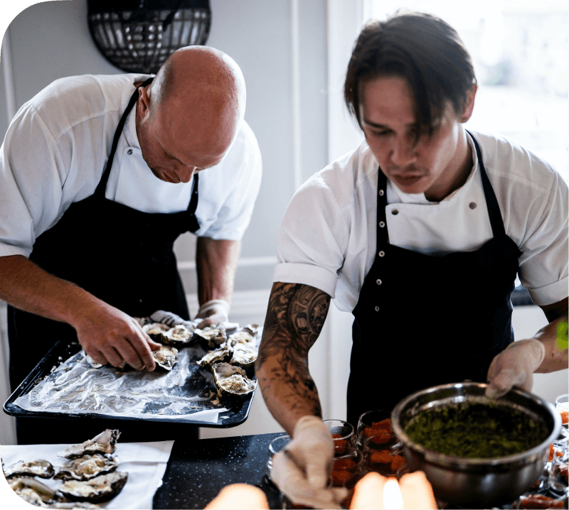 Two chefs preparing oysters at a catering company.