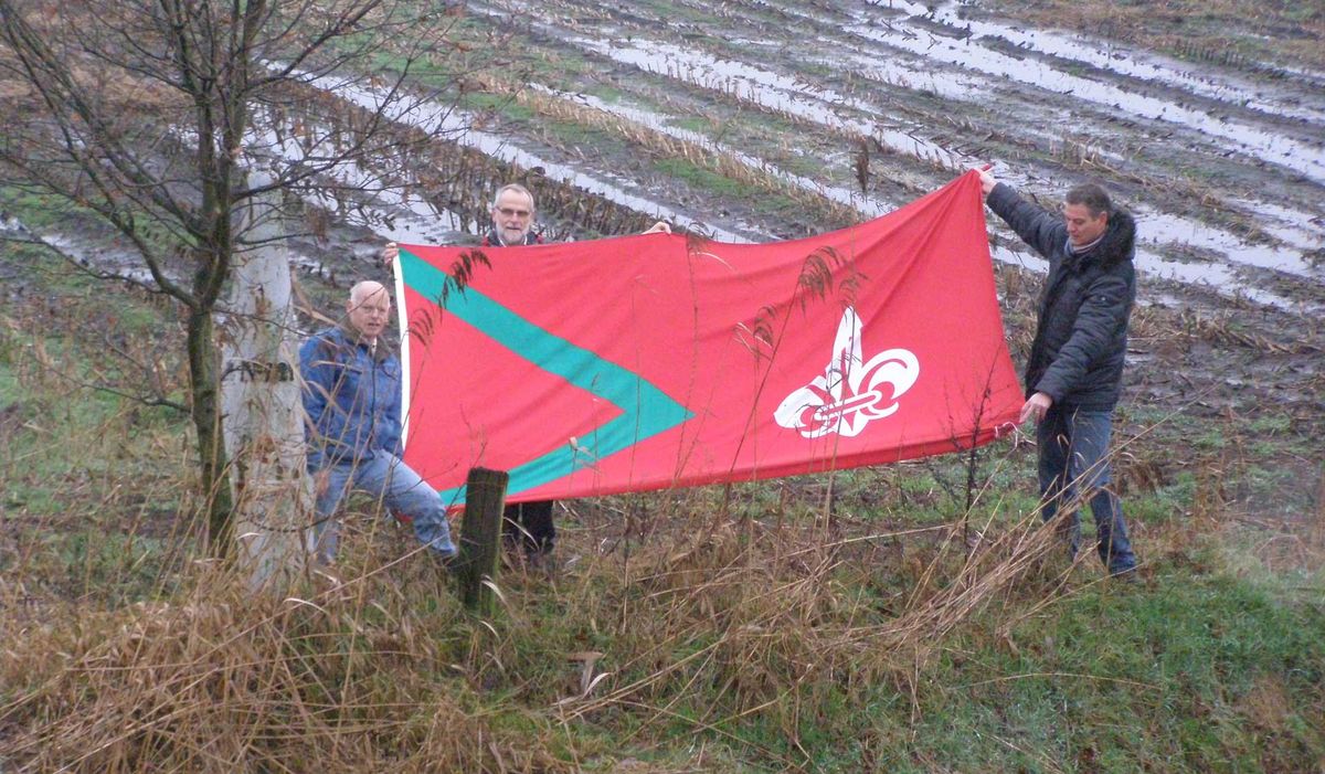 Initiatiefnemer Mike in ’t Groen (midden) samen met Jan Bastiaansen (links) en Toine Graumans (rechts) met de Rijsbergse vlag bij Grenspaal nr. 221 op de grens van Zundert-Rijsbergen-België (foto: Charles Luijten)
