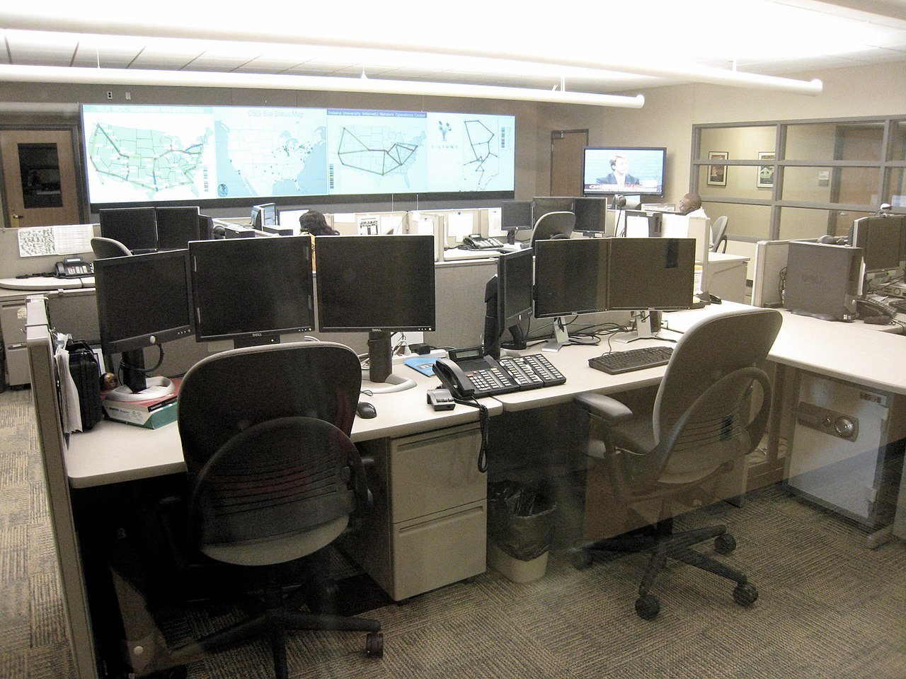 Network operations staff monitoring workstations and large displays in an office operations center