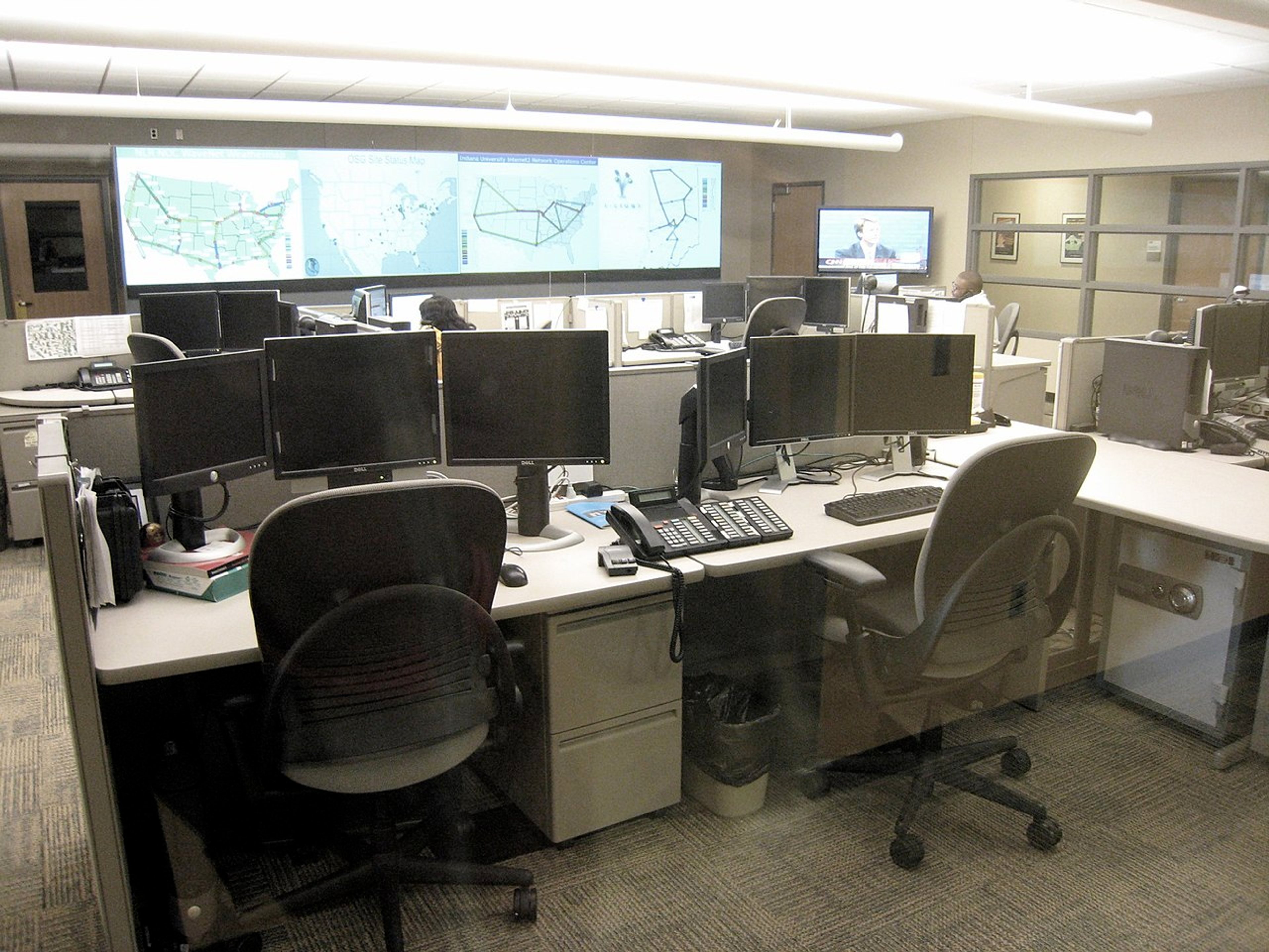 Network operations staff monitoring workstations and large displays in an office operations center