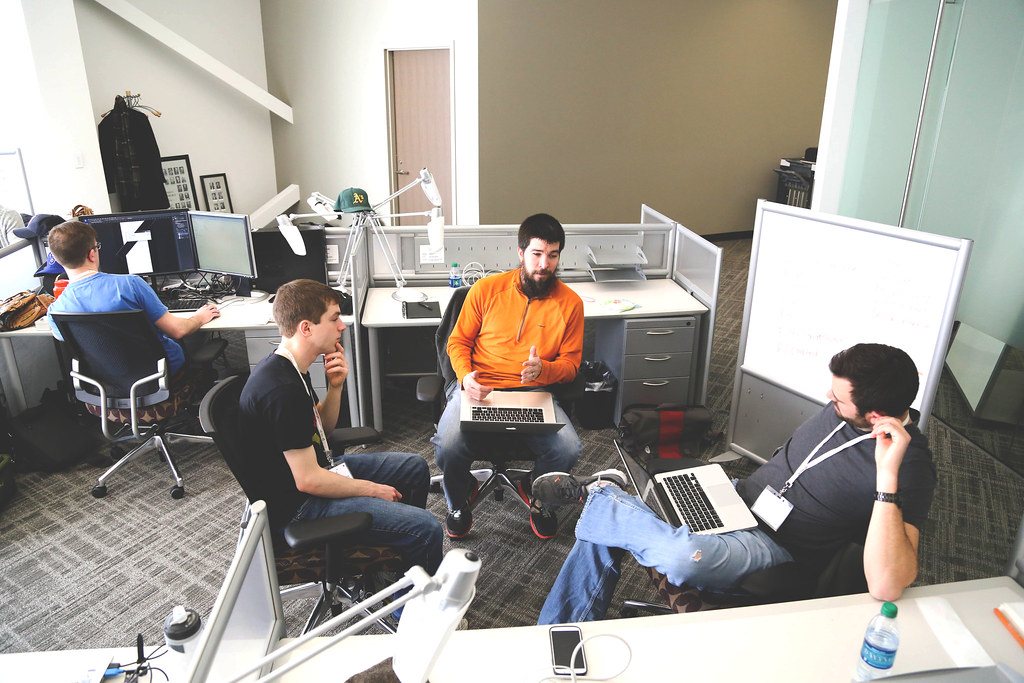 IT professionals discussing workflow intake around laptops in a small business office