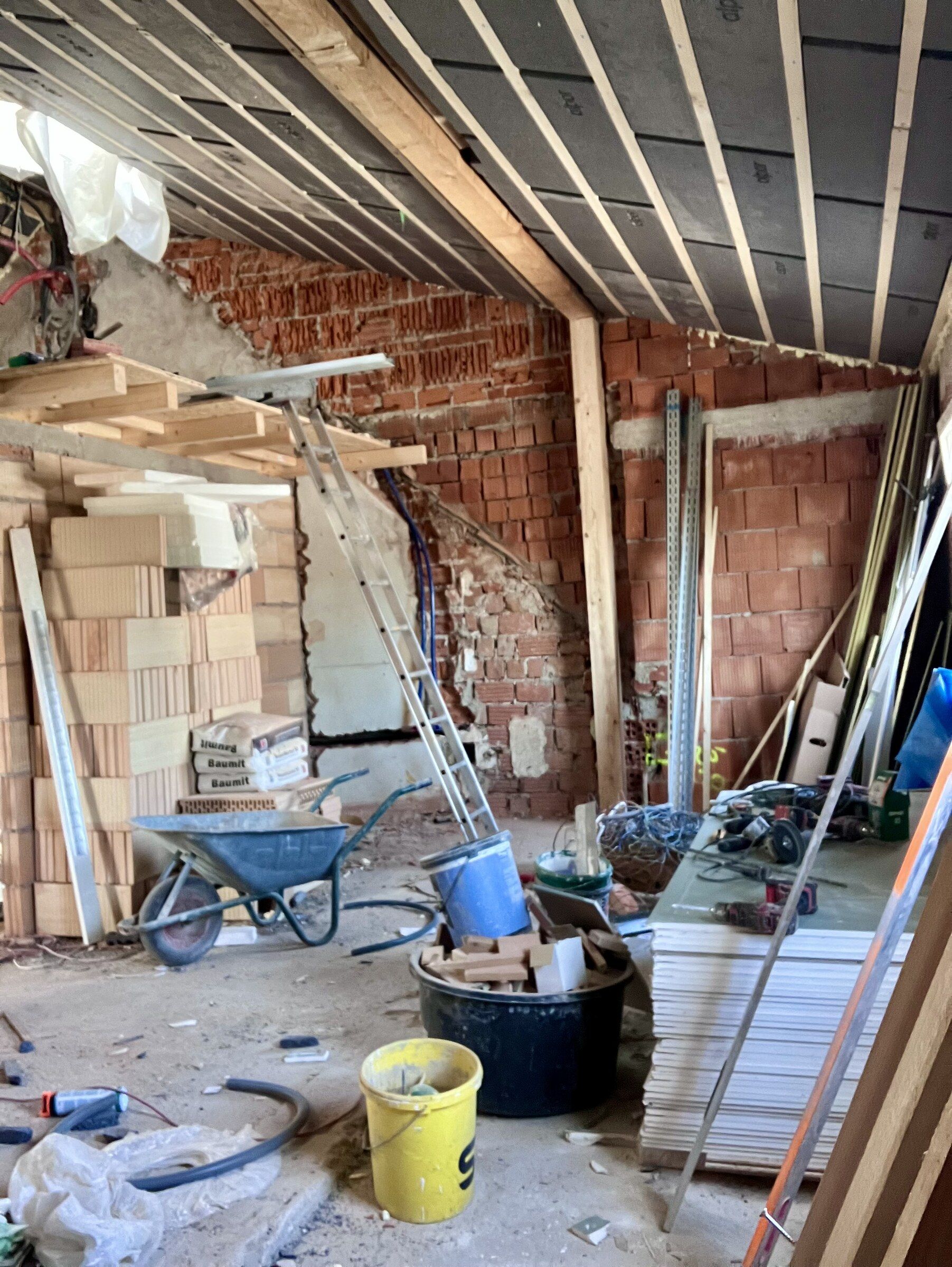 Rohbau des künftigen Praxisraums mit Ziegelwänden, Dachbalken und Baumaterial