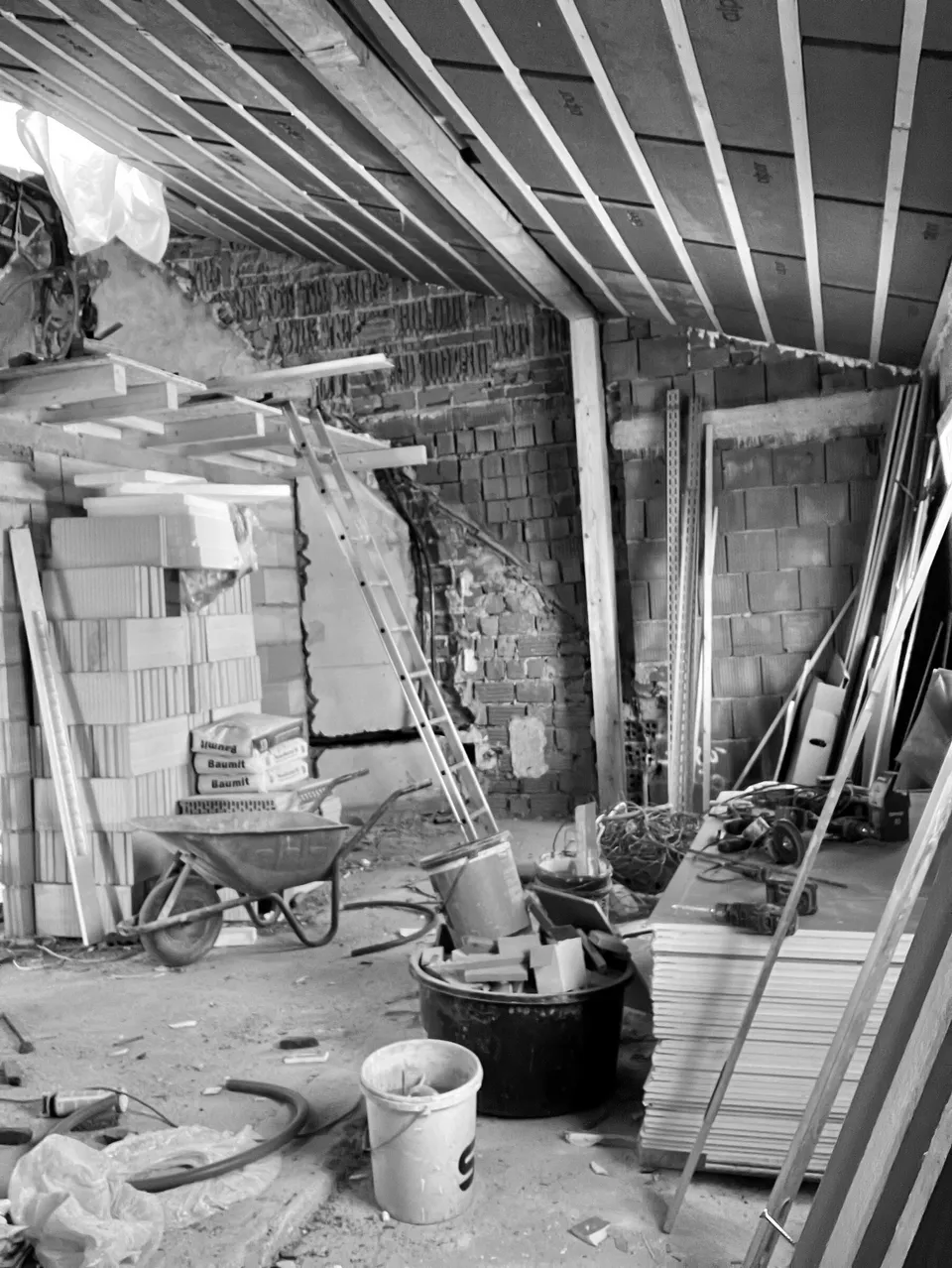 Rohbau des künftigen Praxisraums mit Ziegelwänden, Dachbalken und Baumaterial