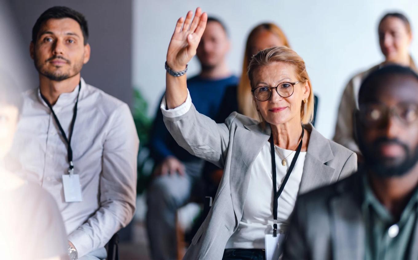 A woman raising her hand in a training session, colleagues seated around her