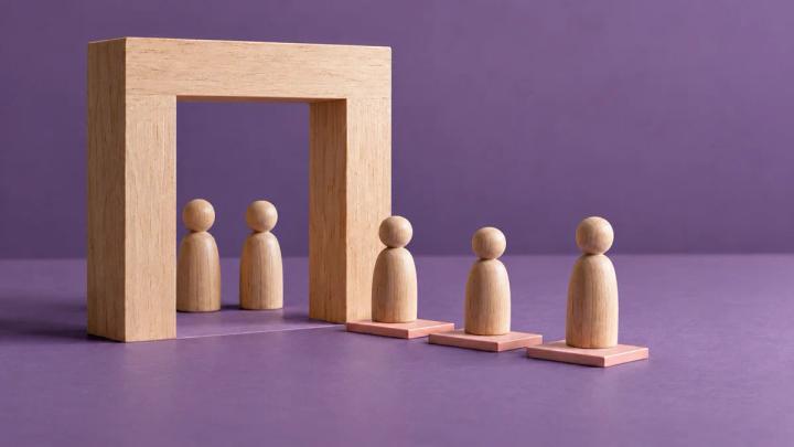 Wooden figures standing in a line beside a wooden doorway against a purple background