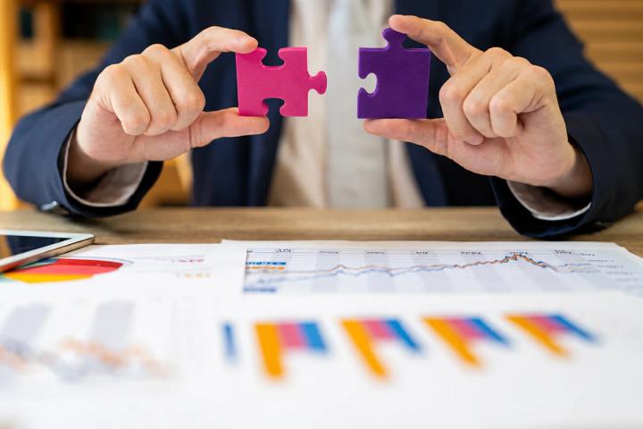 Two hands holding separate pink and purple puzzle pieces above business performance charts