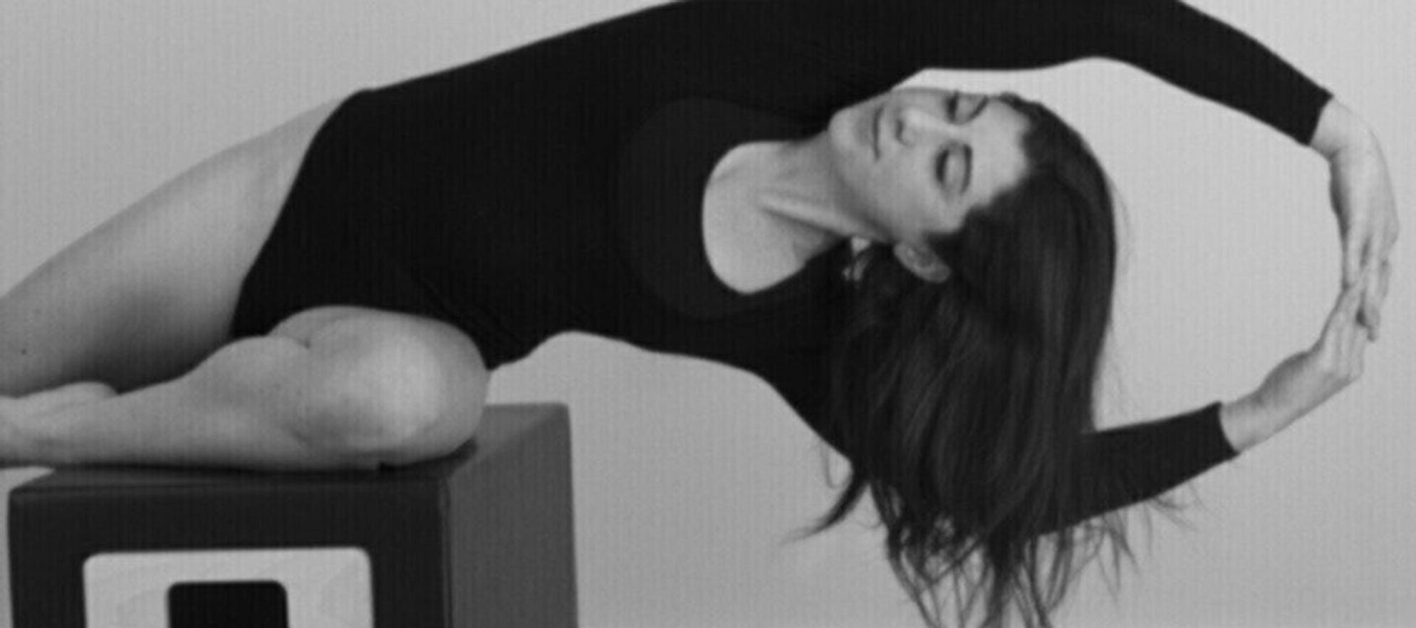 a woman with dark hair doing pilates in a black leotard