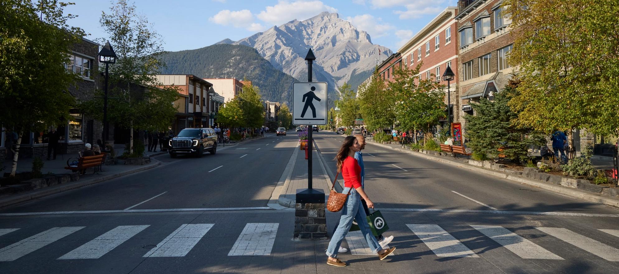 Two people crossing the road in downtown Banff with a mountain in the background.