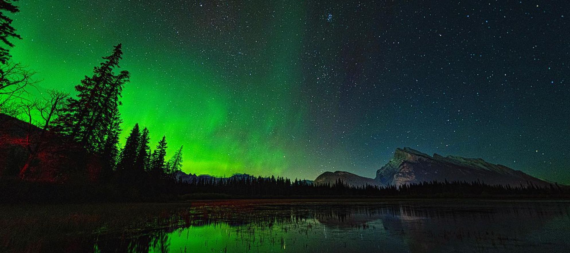 Green aurora glowing over mountains near at Vermilion Lakes in Banff National Park
