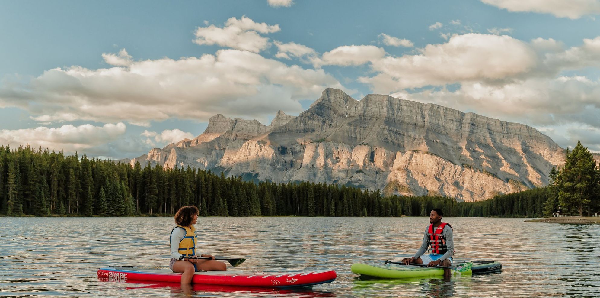 Couple on paddleboards in the middle of the lake; Rundle in Background