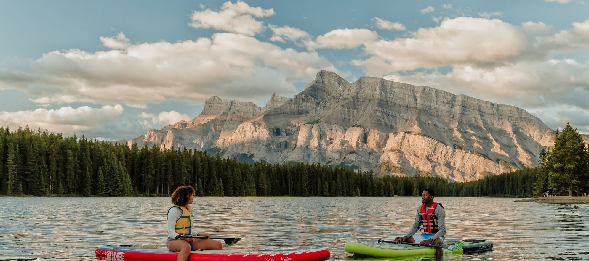 Couple on paddleboards in the middle of the lake; Rundle in Background