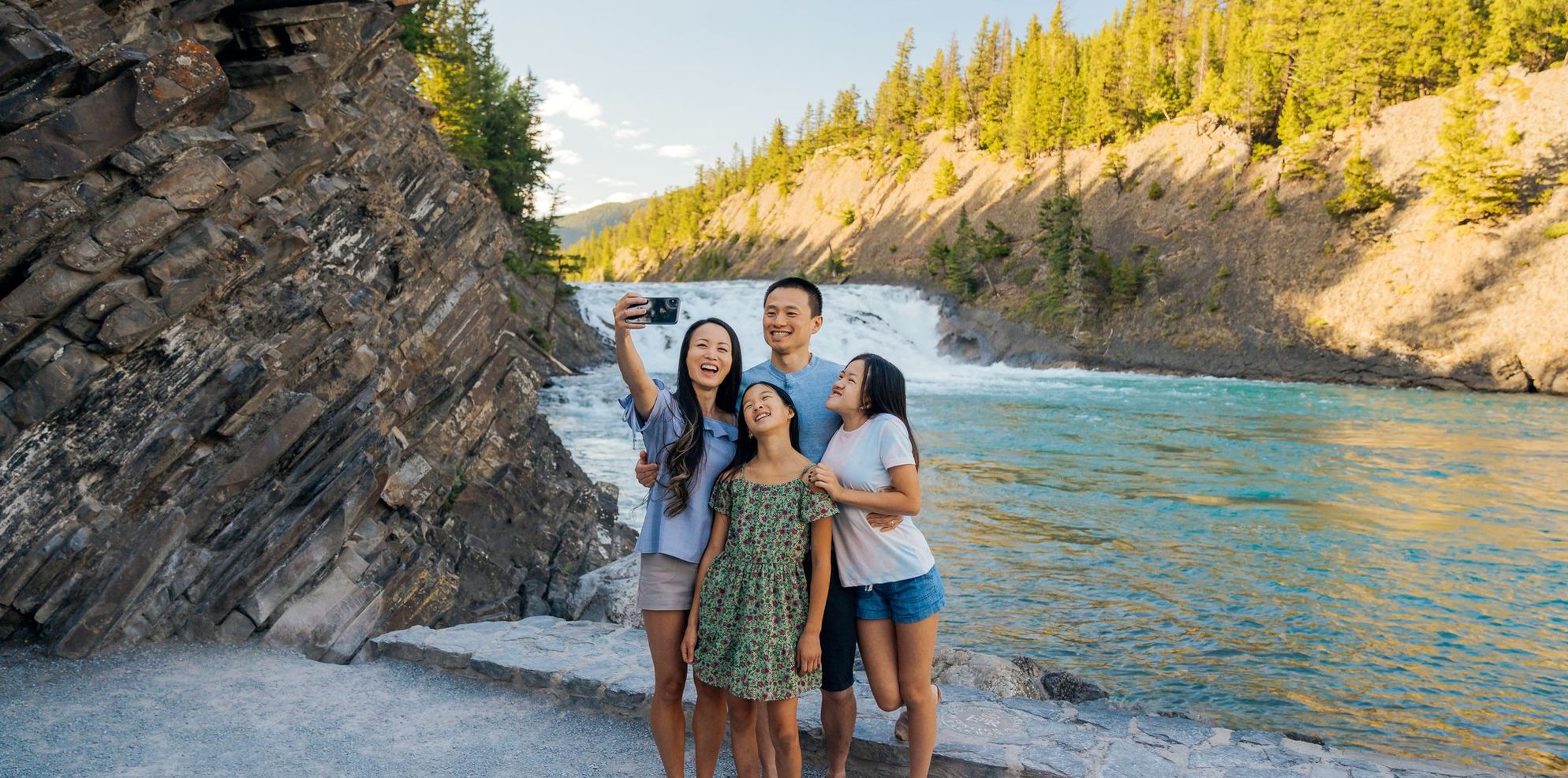 A family of four take a selfie in front of a small waterfall on a sunny summer day