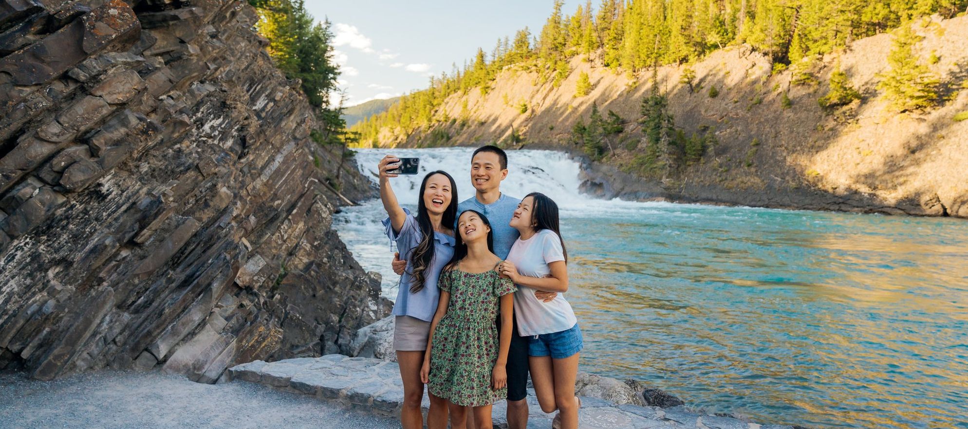 A family of four take a selfie in front of a small waterfall on a sunny summer day