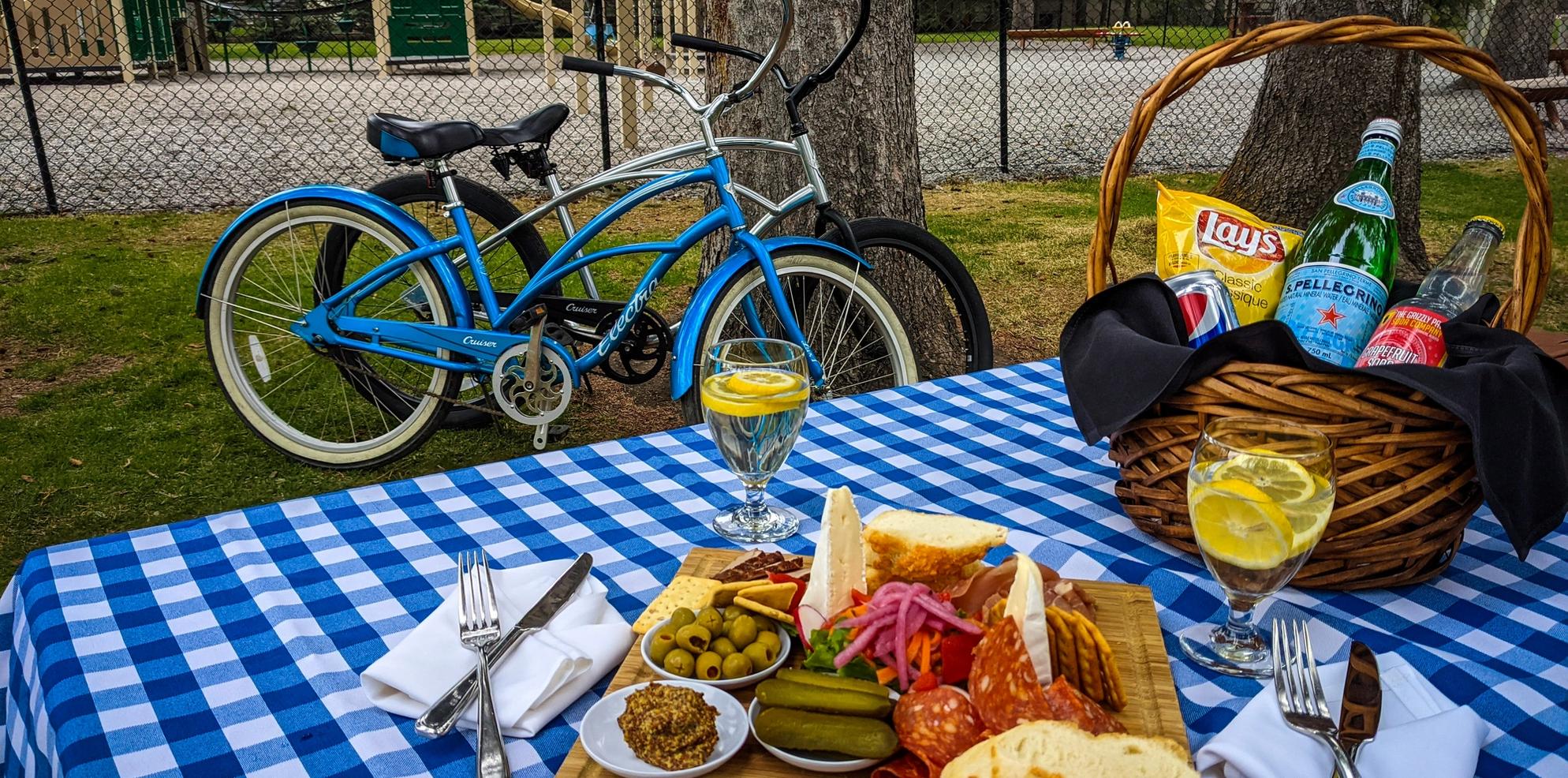 A picnic spread including a charcuterie board and sparkling water on a blue checkered blanket