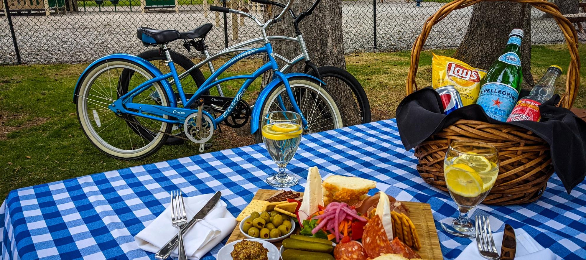A picnic spread including a charcuterie board and sparkling water on a blue checkered blanket