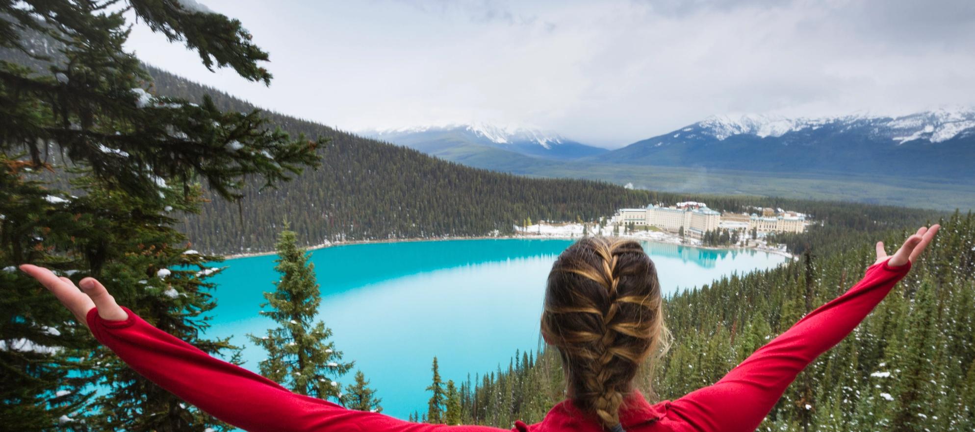Woman meditating at Lake Louise with a view of the lake and Fairmont Chateau Lake Louise.