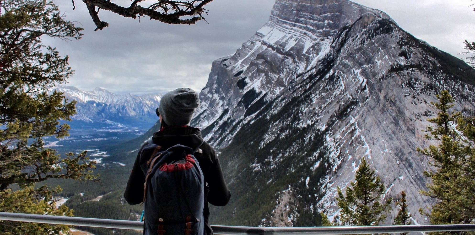 A woman stands on Tunnel Mountain looking towards Mountain Rundle surrounded by trees in Banff National Park.